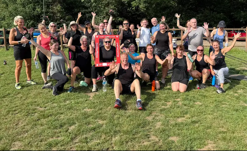 A big Bootcamp BR2 group waving on the grass at the rugby club in Bromley, one holding a #bootcampbr2 frame