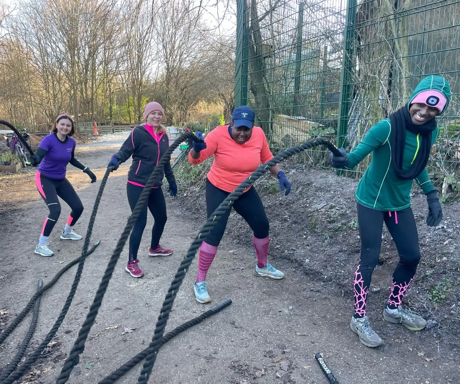 Four Bootcamp SE16 members working battle ropes on the path at Stave Hill on a cold winter morning, laughing
