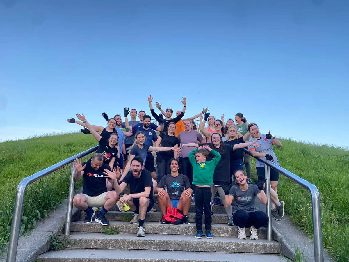 A Bootcamp SE16 group with their arms in the air on the Stave Hill steps under a clear blue sky