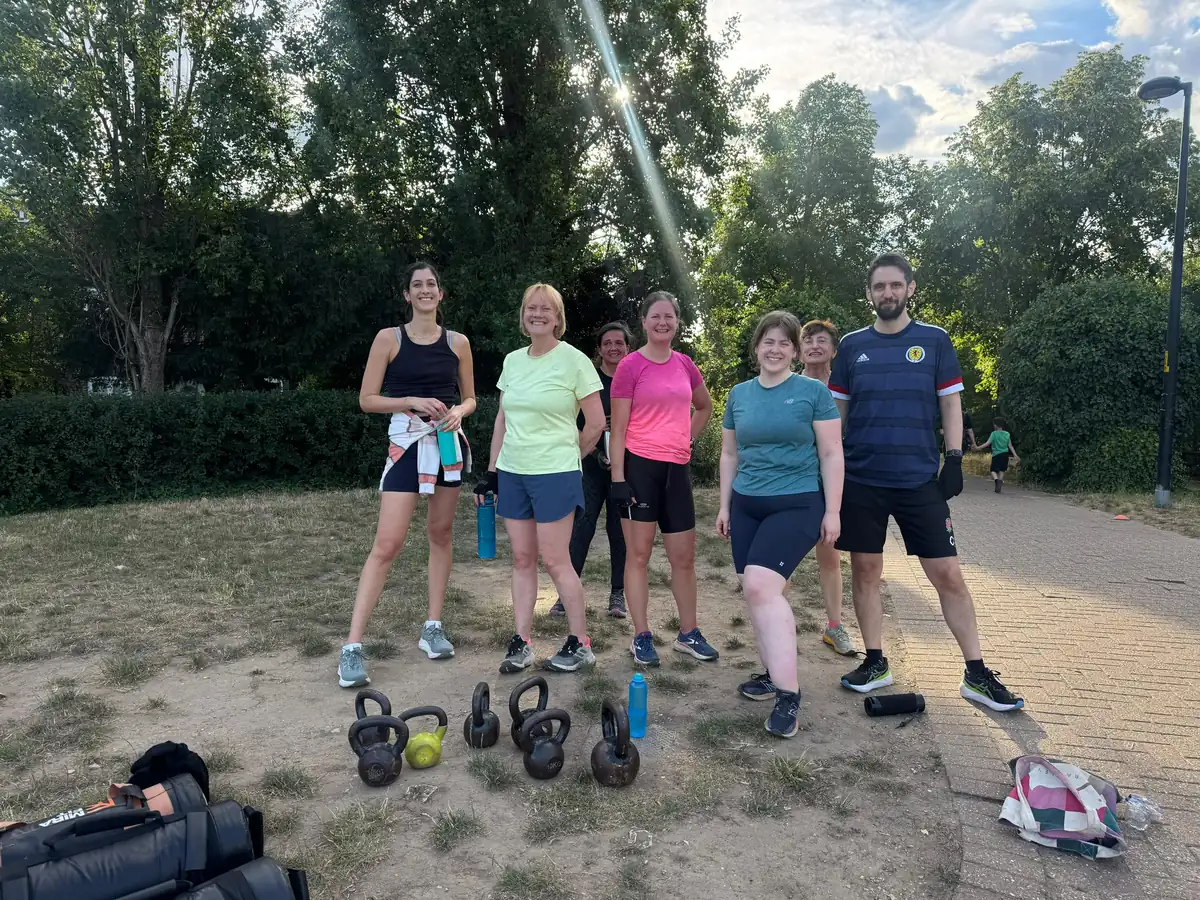 Six members standing behind a row of kettlebells before an evening strength session