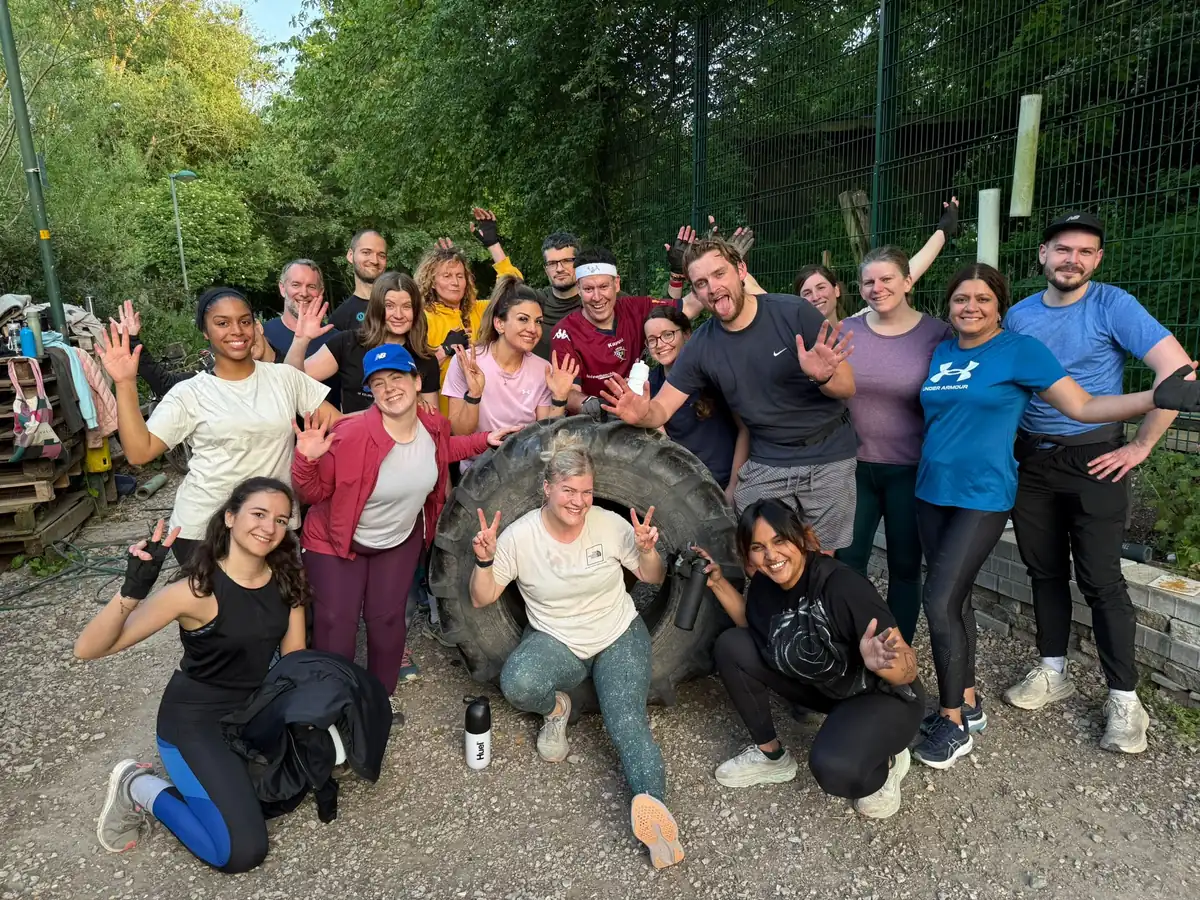 A Bootcamp SE16 group gathered round a tractor tyre among the trees at Stave Hill after a session