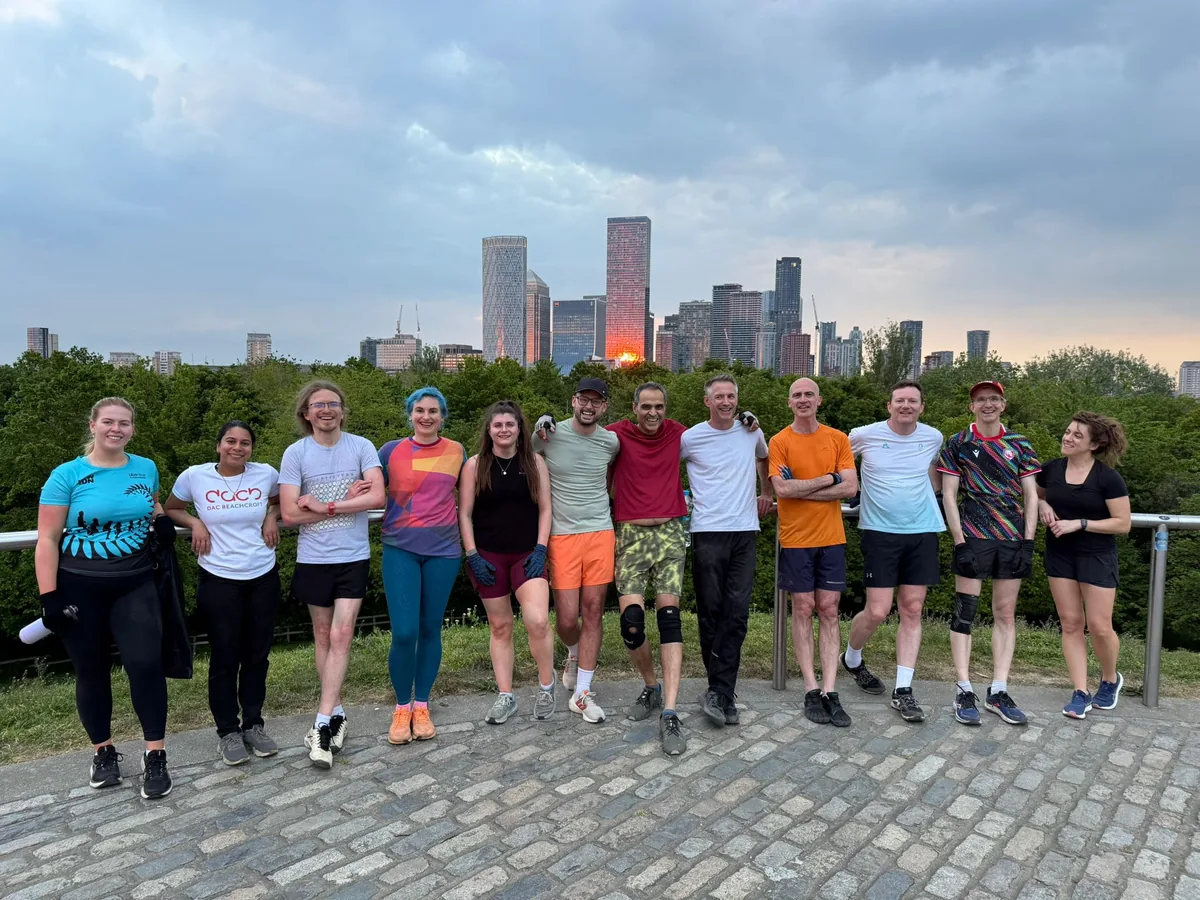 A large Bootcamp SE16 group standing together at the top of the Stave Hill steps at dusk, with the Canary Wharf skyline behind them