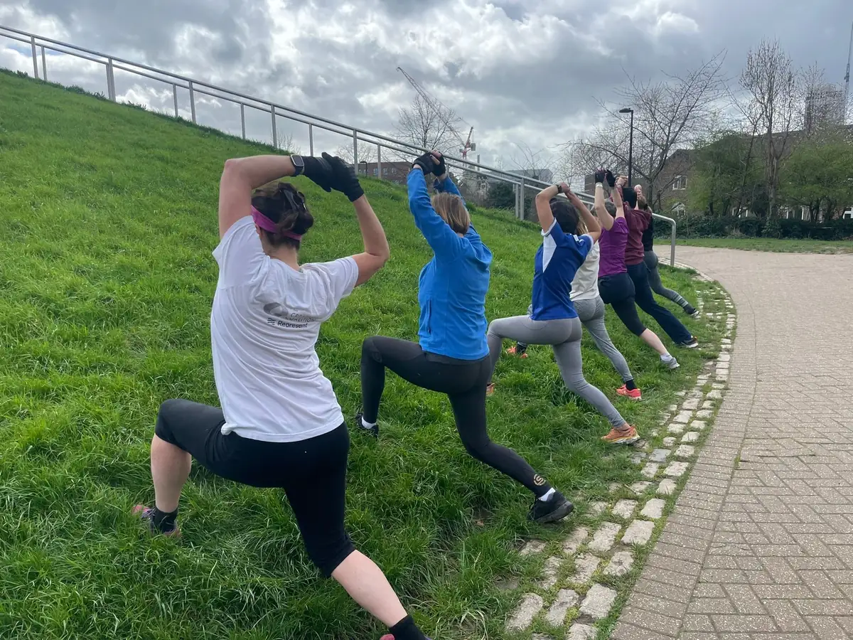Bootcamp SE16 members doing overhead lunges in a line on the grass beside the path at Stave Hill