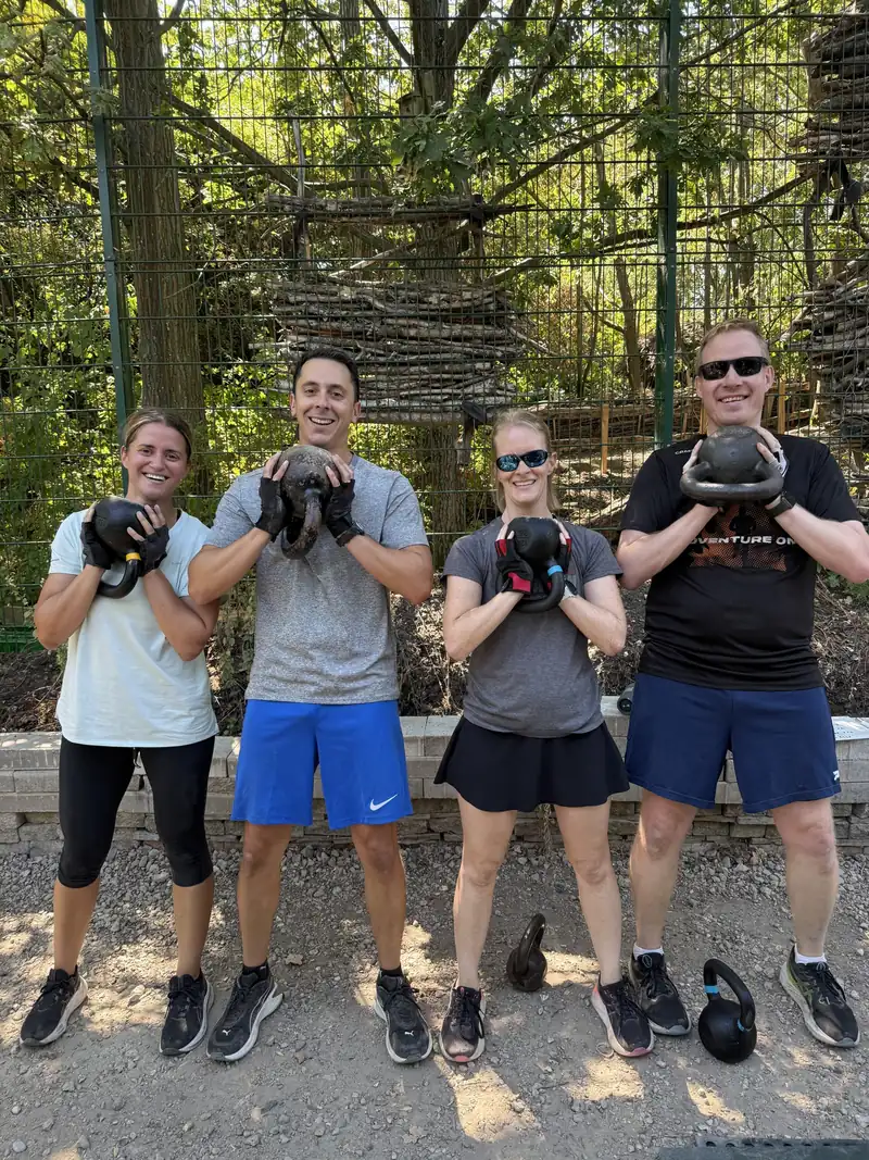 Four Bootcamp SE16 members holding kettlebells by the shed at Stave Hill, smiling at the camera