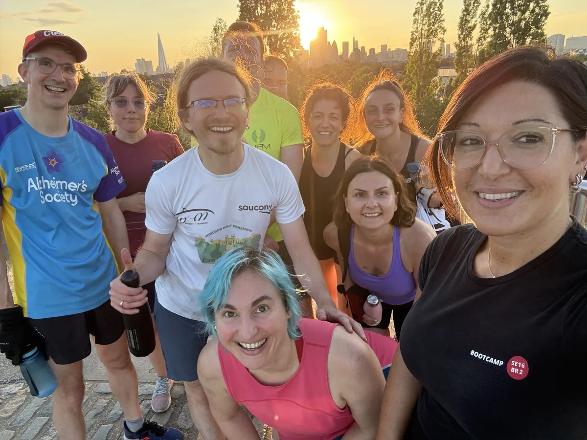Steph and a group of members grinning in a selfie on top of Stave Hill, with the sun going down behind the Shard