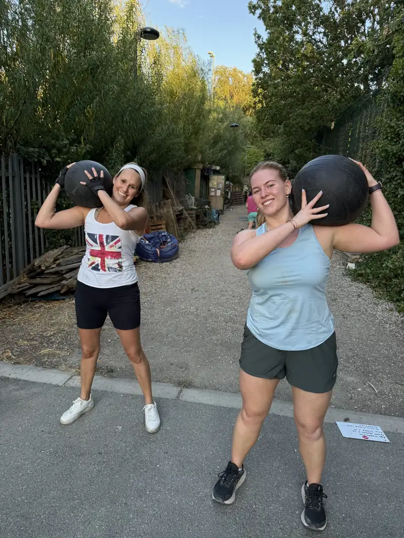 Two members laughing with slam balls on their shoulders on the path at Stave Hill