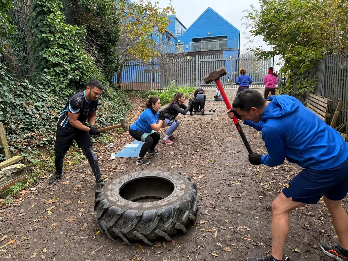 Bootcamp SE16 members swinging sledgehammers onto tractor tyres along the path by the shed