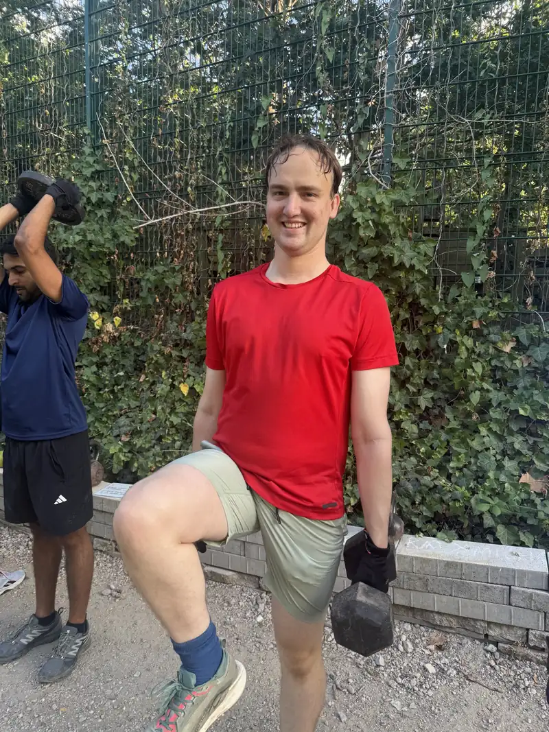 A member grinning mid step-up with dumbbells on the path at Stave Hill