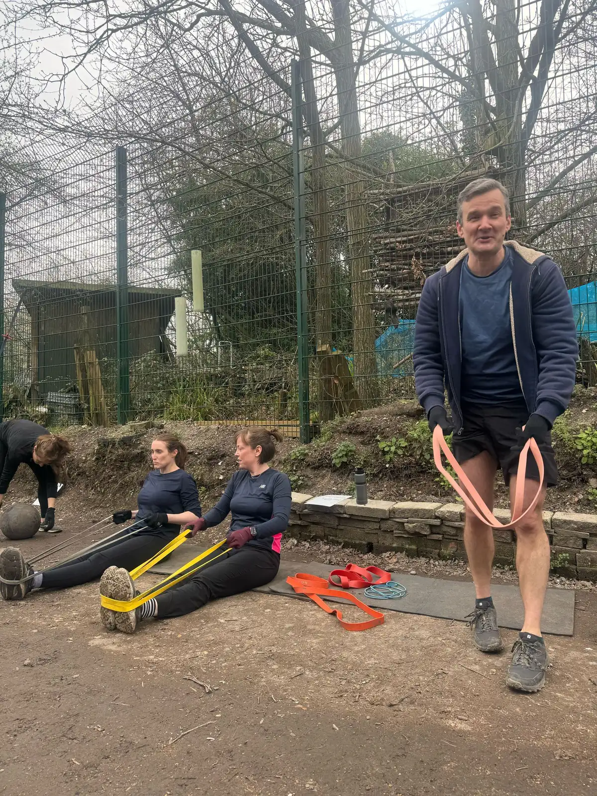 A coach guiding members through resistance band work outdoors on a cold morning