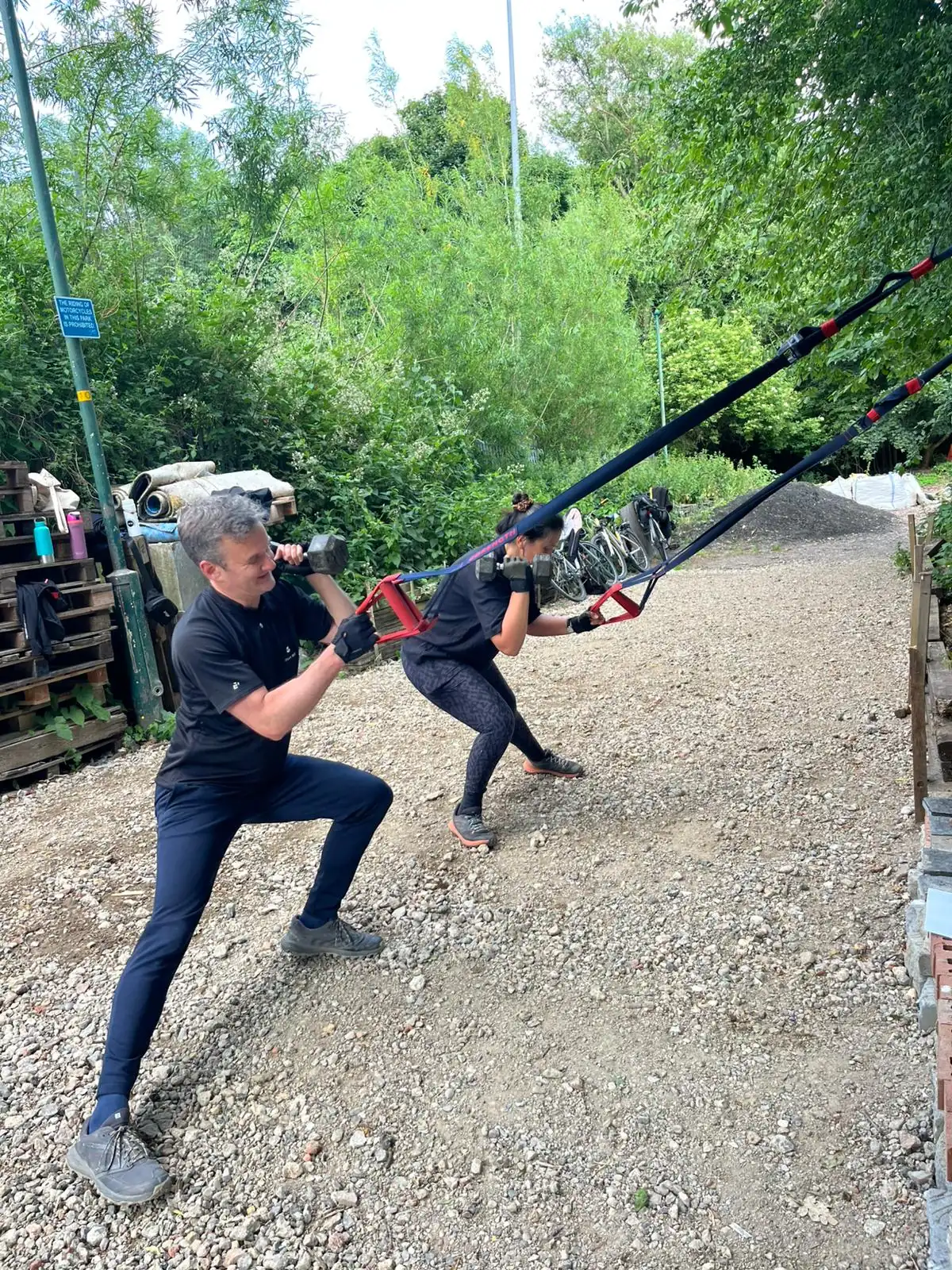 A member working through a TRX exercise outdoors while a coach watches the movement
